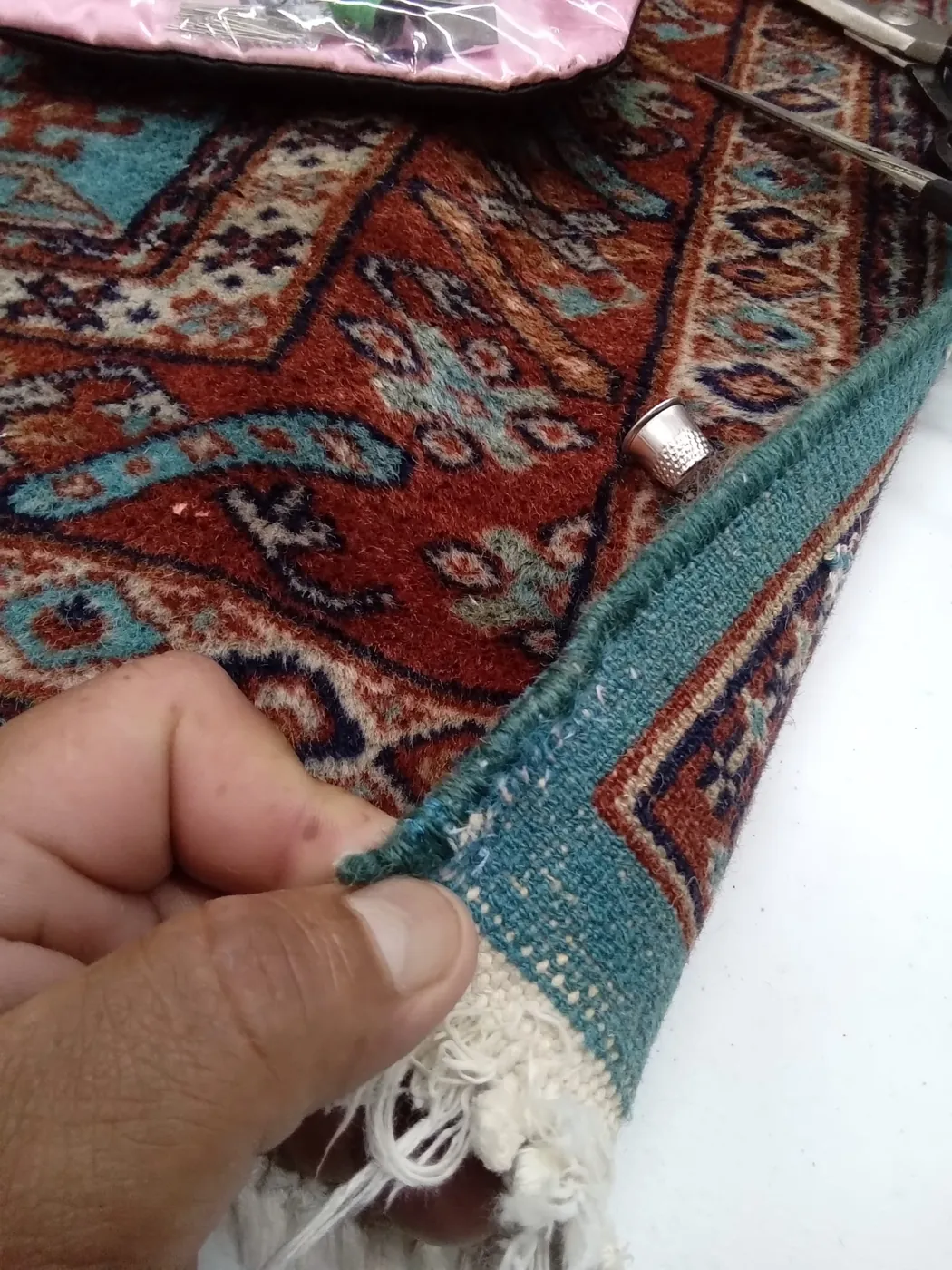 Hands working the red fringe of a rug at the repair bench